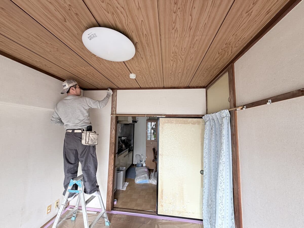 脚立に上がって天井際のクロスを施工しているところ